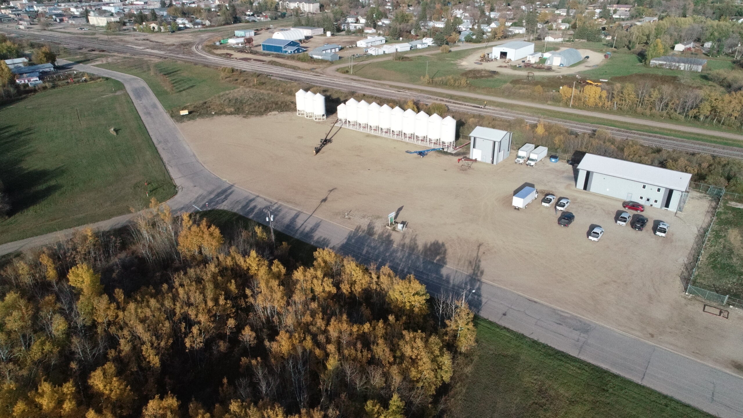 Photograph of the New Era Ag property. Foreground is green grass and a large sign with the New Era Ag logo. Background is the property with road and buildings. Blue sky with clouds.